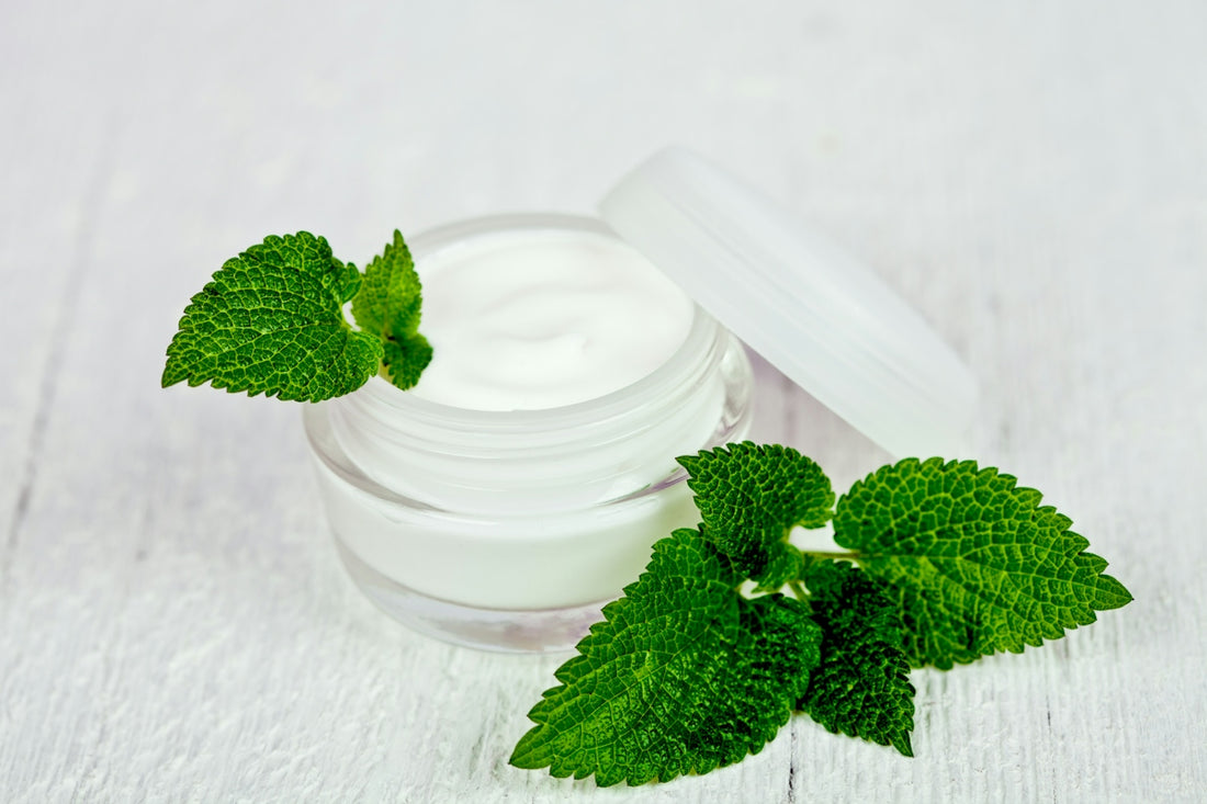 A jar of cream with mint leaves on a white table