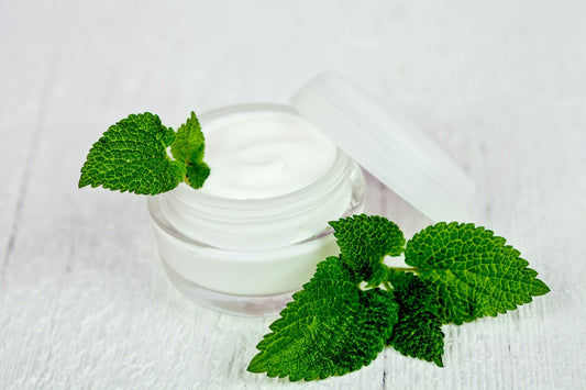 A jar of cream with mint leaves on a white table